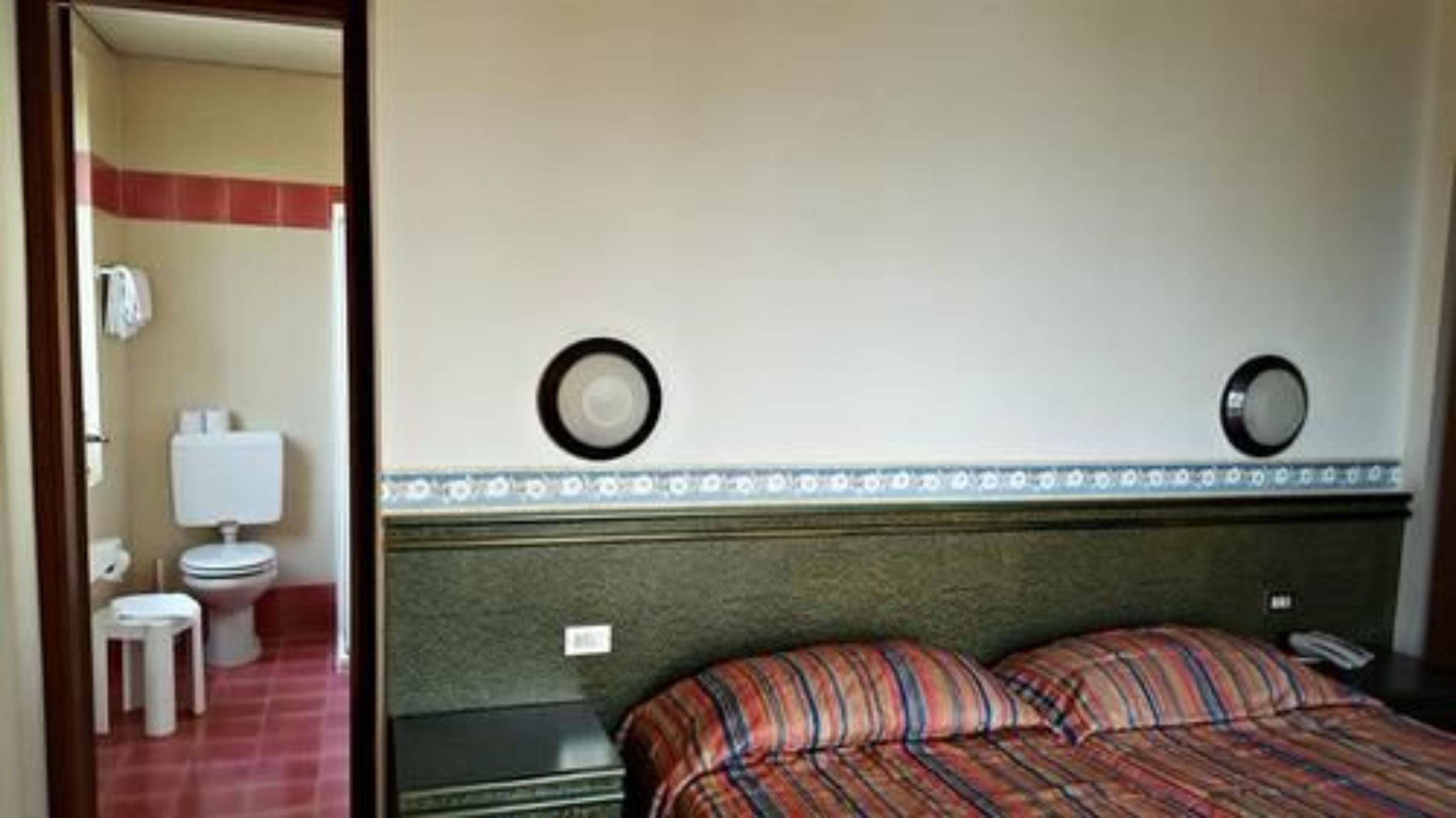 A hotel room with a bed, a small stool, a toilet, and a nightstand.