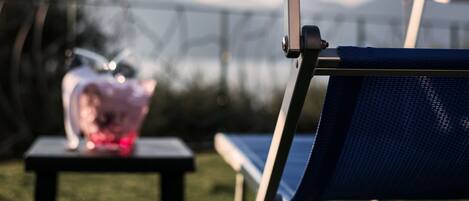 A blue outdoor chair with a metal frame, a small table with a pink object, and a blue umbrella in the background.
