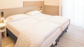 Una cama doble con ropa blanca, cabecera de madera, mesitas de noche y suelo de madera claro.