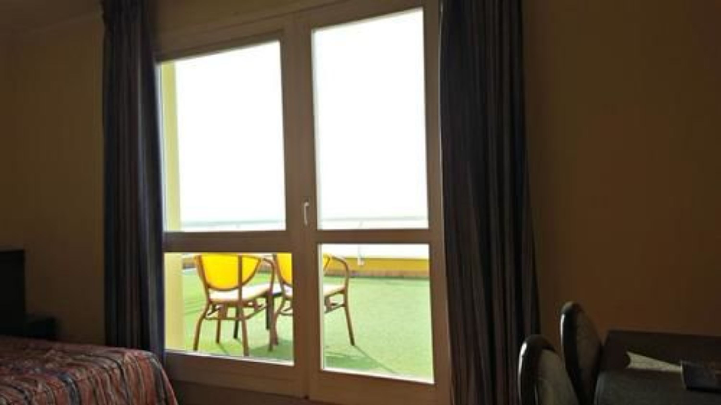 A hotel room with a large sliding glass door leading to an outdoor area with chairs and a table.