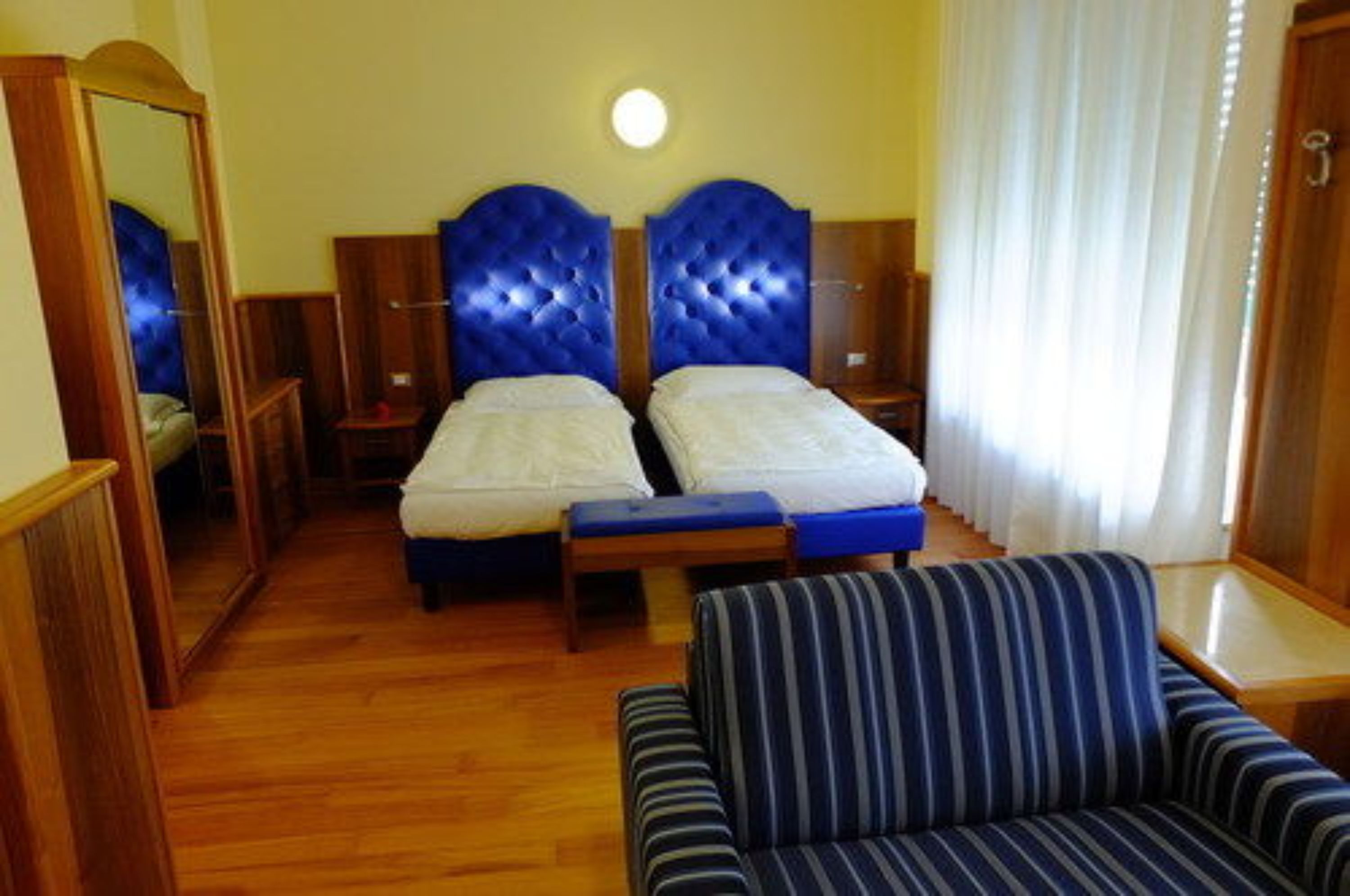 A hotel room with two beds, a wooden floor, a striped sofa, and a mirror.