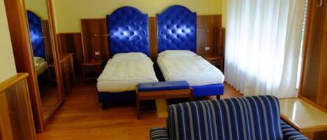 A hotel room with two beds, a wooden floor, a striped sofa, and a mirror.