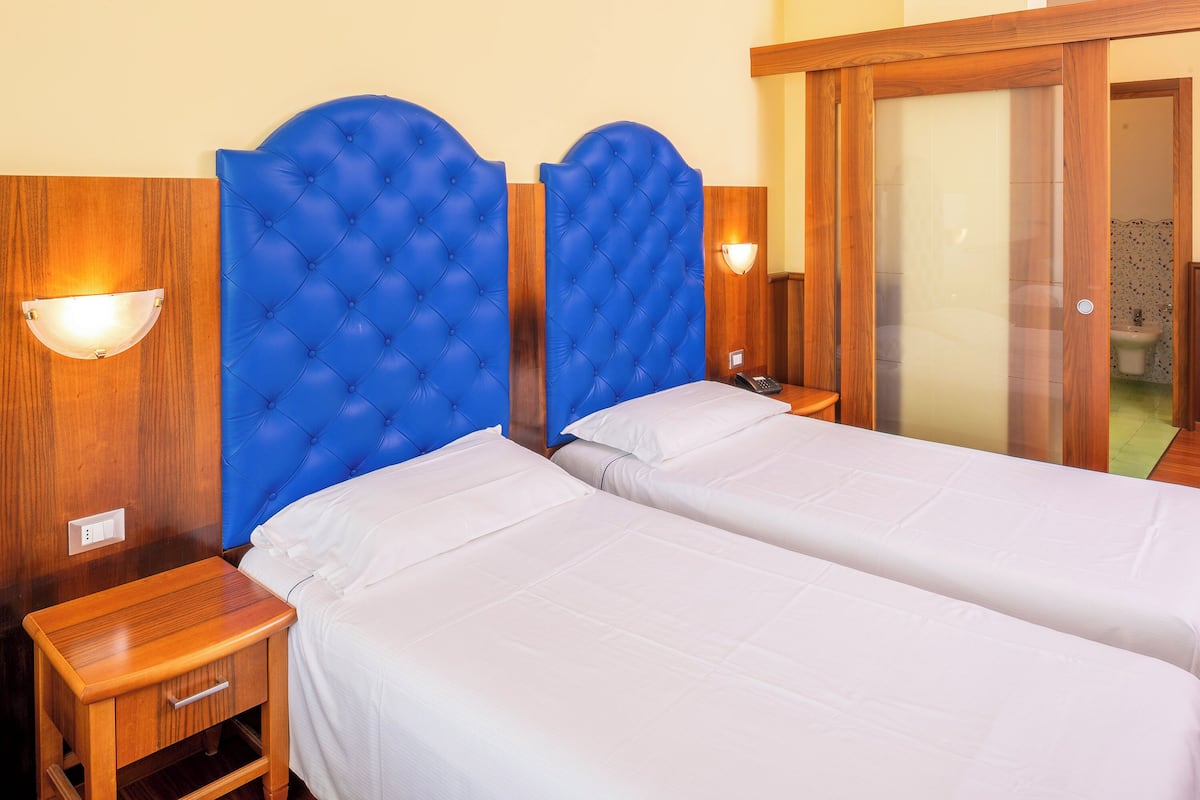 A hotel room with two beds, wooden headboards, and bedside tables with lamps.