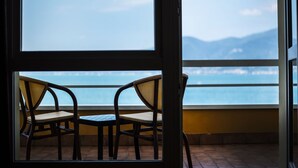 A balcony with two wicker chairs and a small table, overlooking a body of water and distant mountains. - Hotel Internazionale (Torri del Benaco)