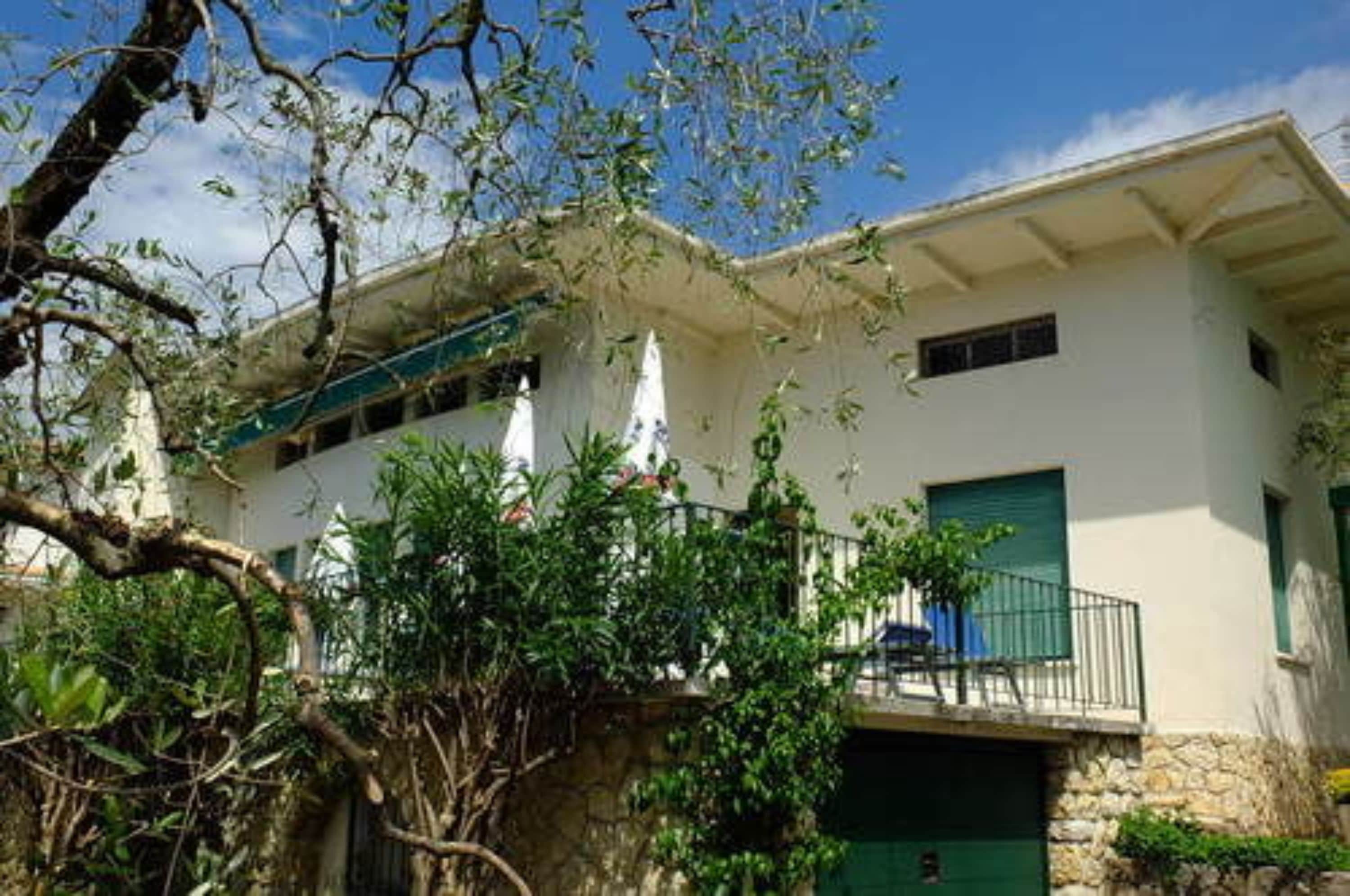 Un edificio de dos pisos con un balcón, un muro de piedra y una puerta verde.