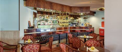 A bar area with wooden bar counters, multiple stools, and a variety of bottles and glasses on shelves.