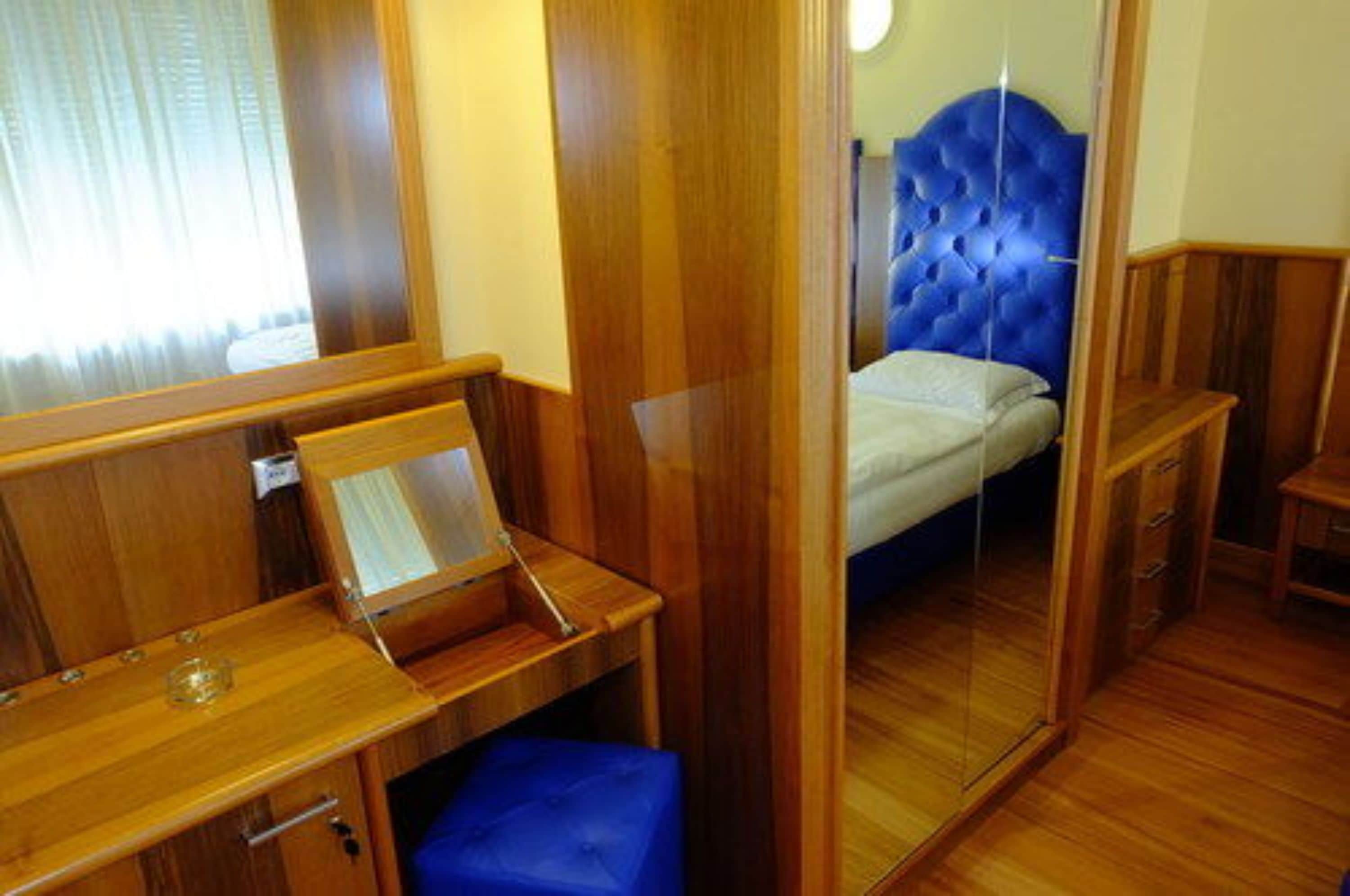 A compact room with a bed, a small desk, and a mirror.