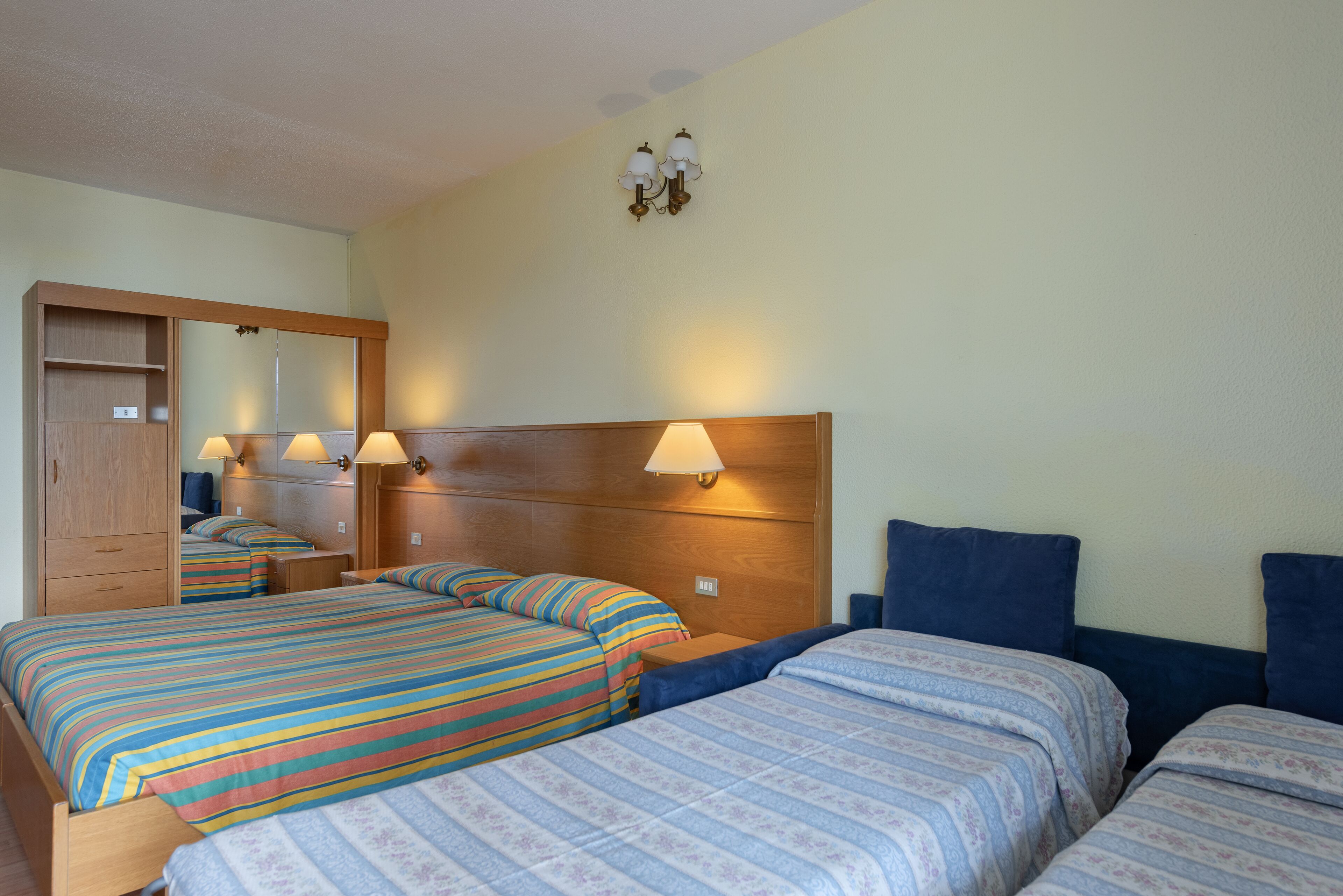 A hotel room with two beds, a wooden wardrobe, and a mirror.