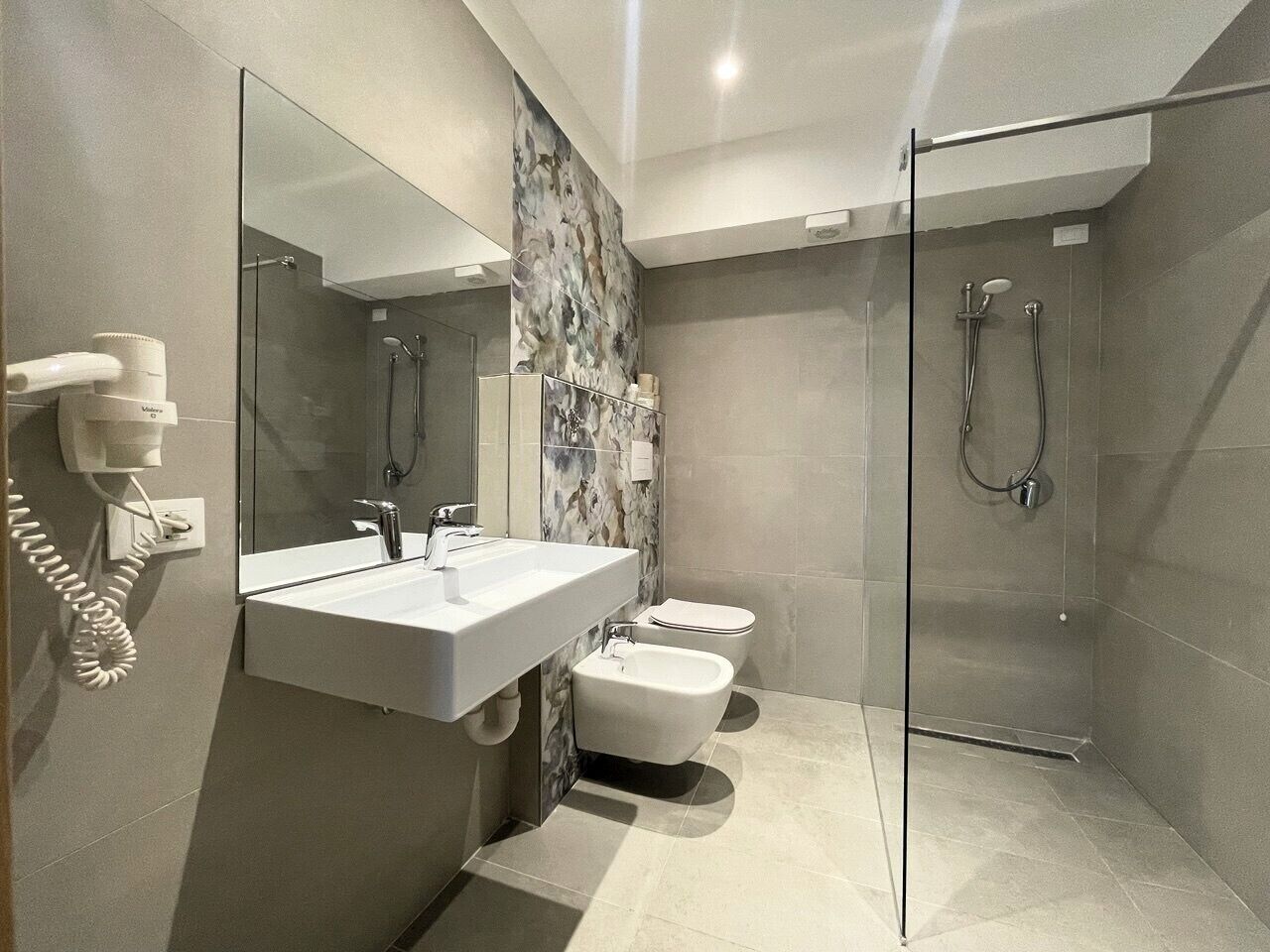 Une salle de bain moderne avec une douche à parois de verre, un lavabo blanc et un bidet.