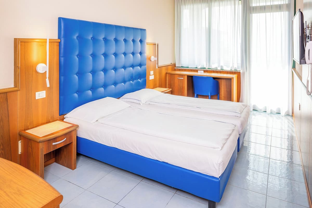 Un dormitorio con cabecera azul, un escritorio de madera, una silla y una cama con ropa blanca.