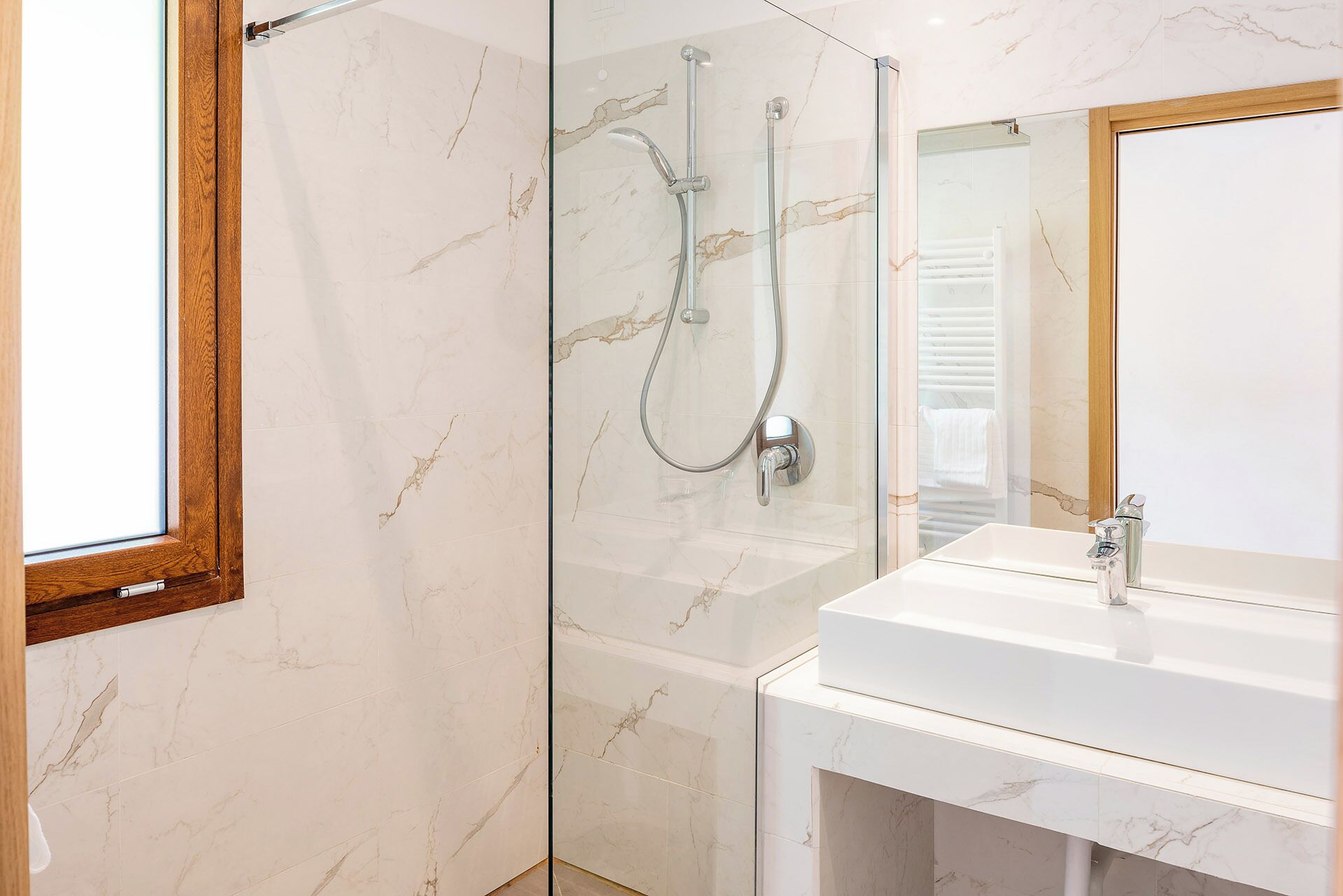 Un baño moderno con cabina de ducha de vidrio, un lavabo blanco y pared con azulejos de mármol.