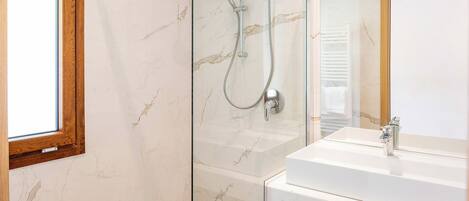 Un baño moderno con cabina de ducha de vidrio, un lavabo blanco y pared con azulejos de mármol.