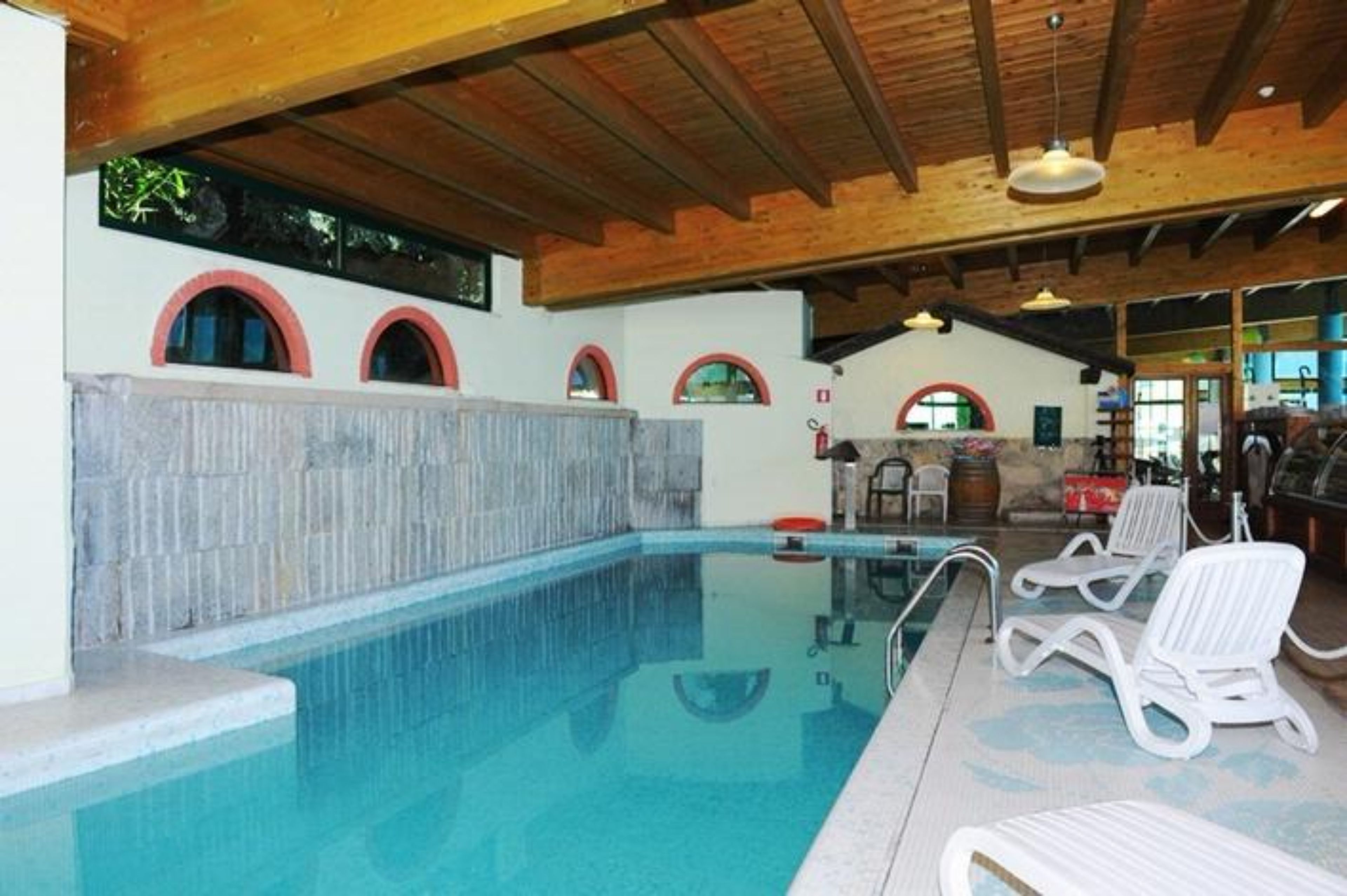 An indoor swimming pool with a stone wall, wooden ceiling beams, and lounge chairs.