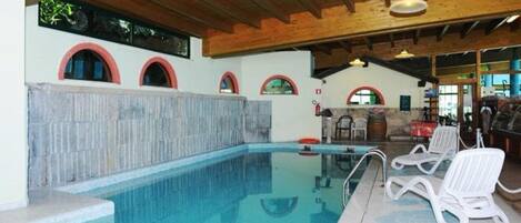An indoor swimming pool with a stone wall, wooden ceiling beams, and lounge chairs.