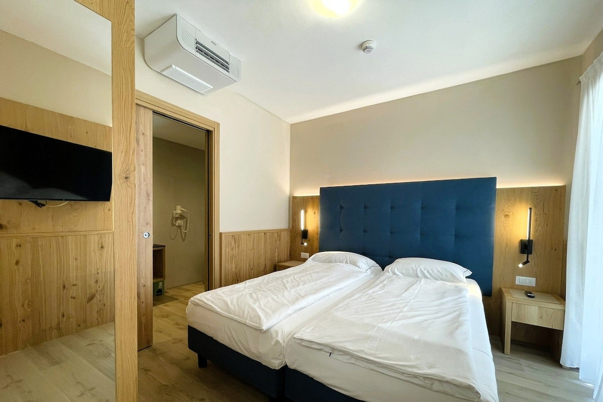 Une chambre d’hôtel avec un lit double, des murs lambrissés, un téléviseur fixé au mur, un appareil de climatisation et une table de chevet avec une lampe.