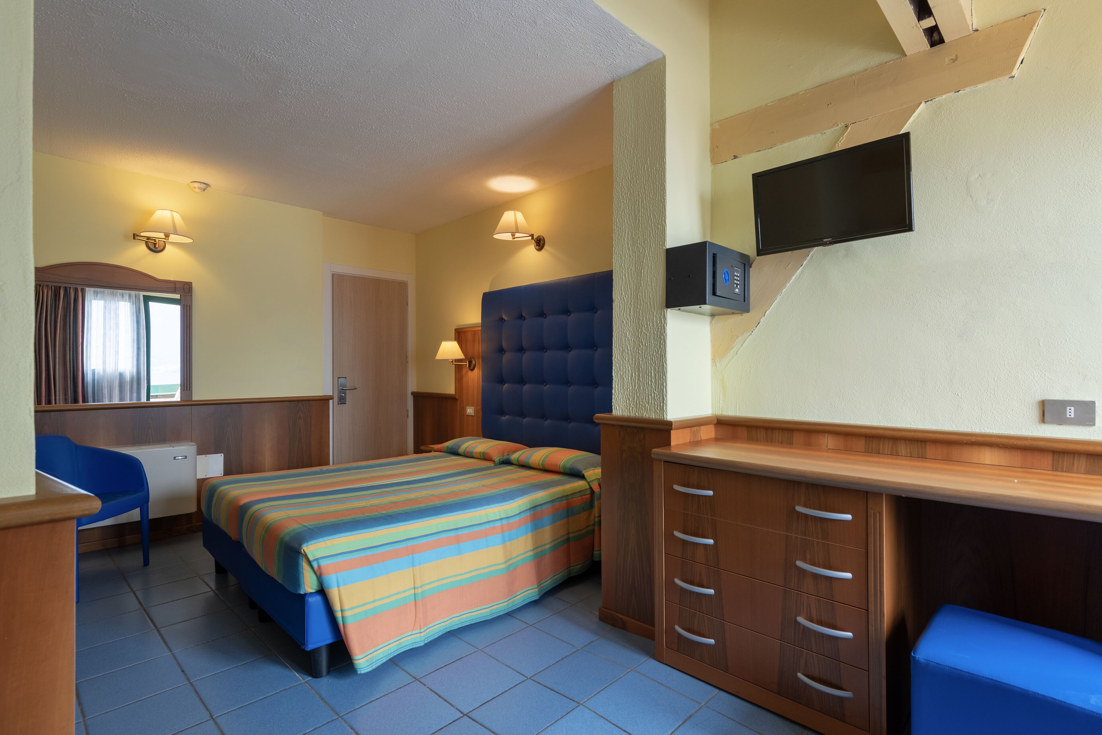 A bedroom with a bed, a desk, a chair, a television, and a wardrobe.