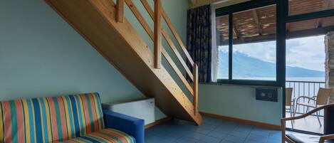 A room with a wooden staircase, a striped sofa, and a view of the sea through a window.