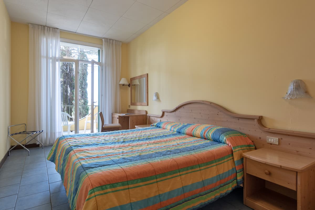 Ein Schlafzimmer mit einem Bett, einem Nachttisch, einem Sessel, einem kleinen Tisch und einem Fenster mit Vorhängen.