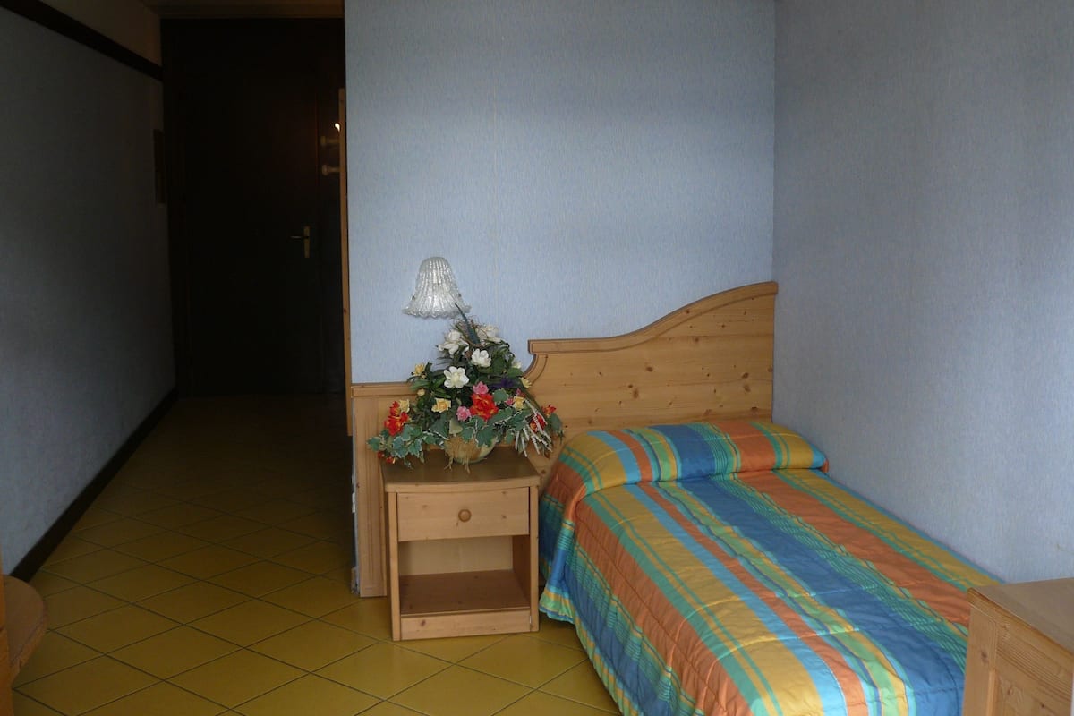 Ein Hotelzimmer mit einem hölzernen Bett, einem Nachttisch mit Lampe und einer Blumenkomposition.