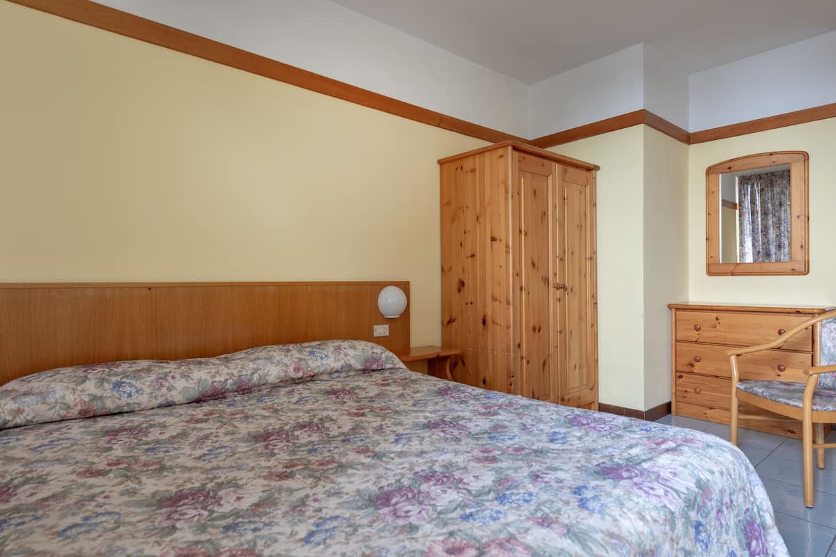 Ein Schlafzimmer mit hölzernem Kopfende, floralem Bettbezug, einem Schrank aus Holz, einer Holzkommode und einem Spiegel an der Wand.