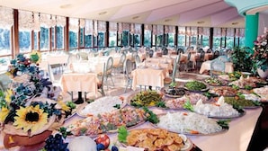 A banquet hall with round tables covered in various dishes, surrounded by chairs. - Hotel Marco Polo (Garda)
