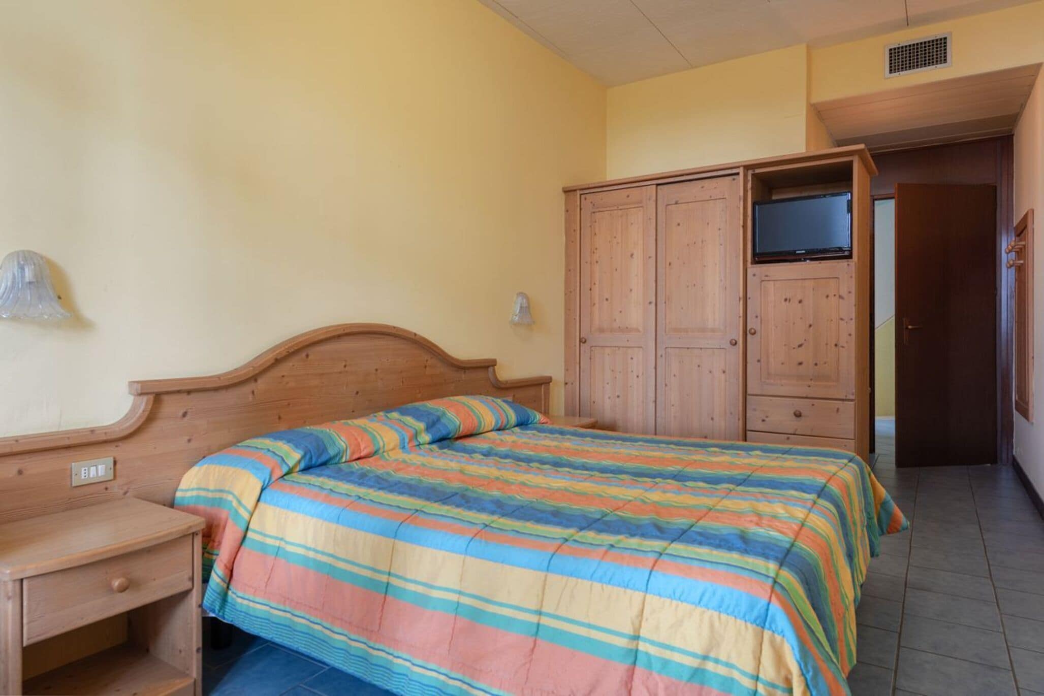 A bedroom with a wooden bed, a nightstand, a wardrobe, and a television.