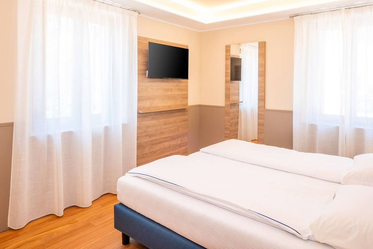 Une chambre d’hôtel avec un grand lit, des boiseries, un téléviseur à écran plat et des rideaux en voile.