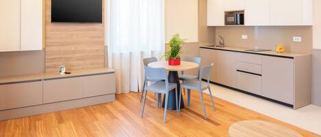 A modern kitchen with a microwave, sink, and cabinets. There is a dining area with a table, chairs, and a potted plant.