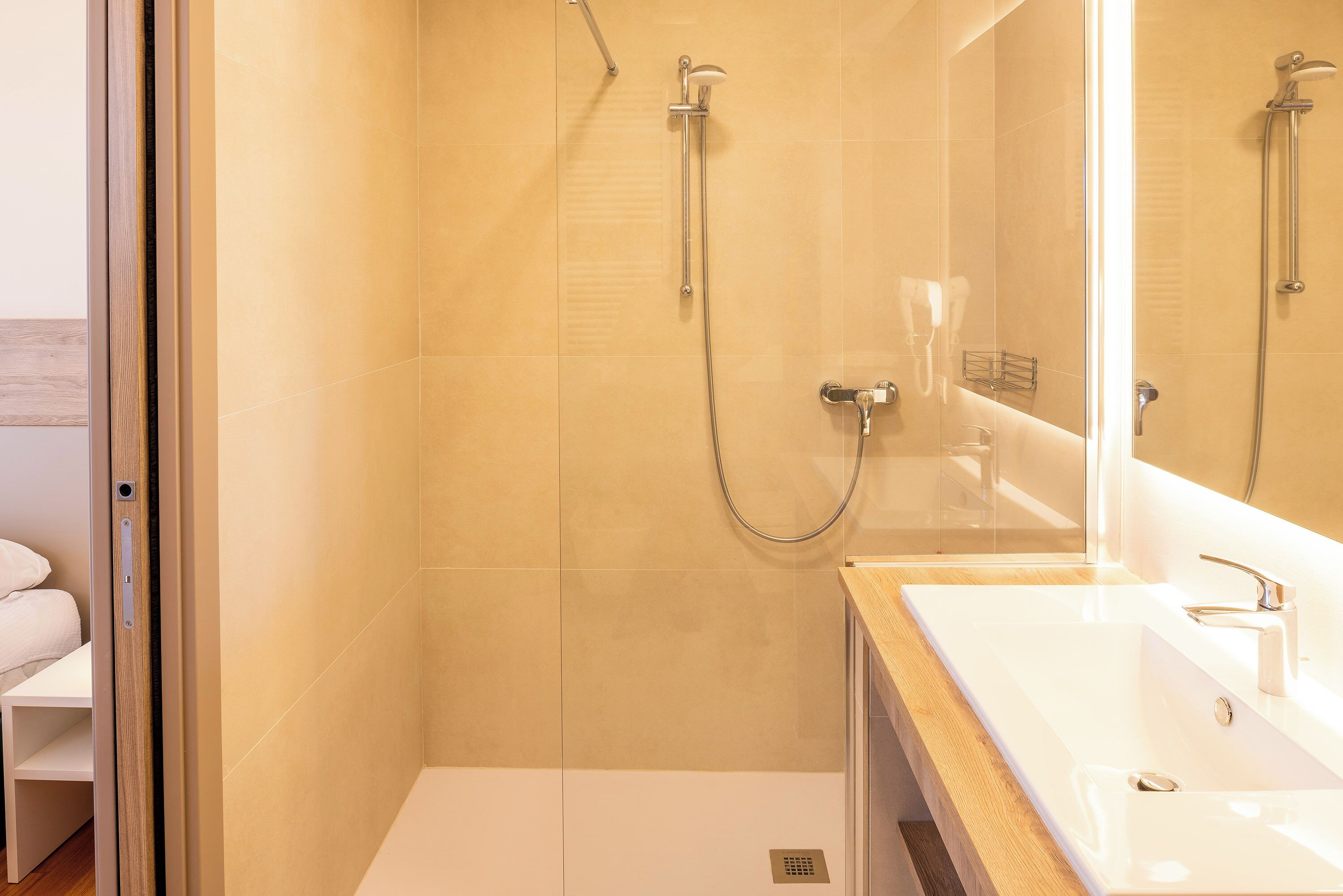 Une salle de bain moderne avec une douche à parois de verre, un lavabo blanc et un grand miroir.