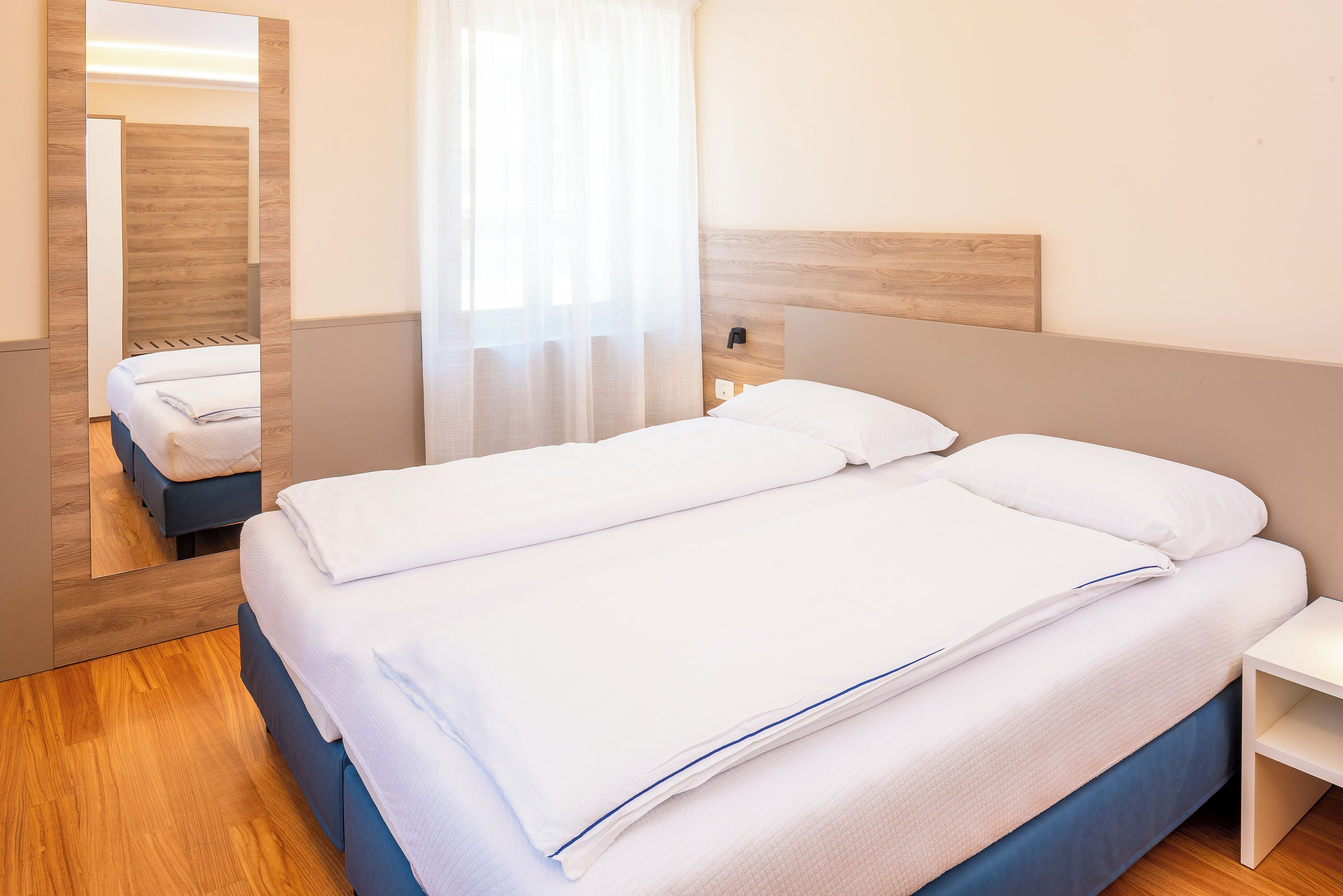 A neatly made bed with white linens, a wooden headboard, and a bedside table.