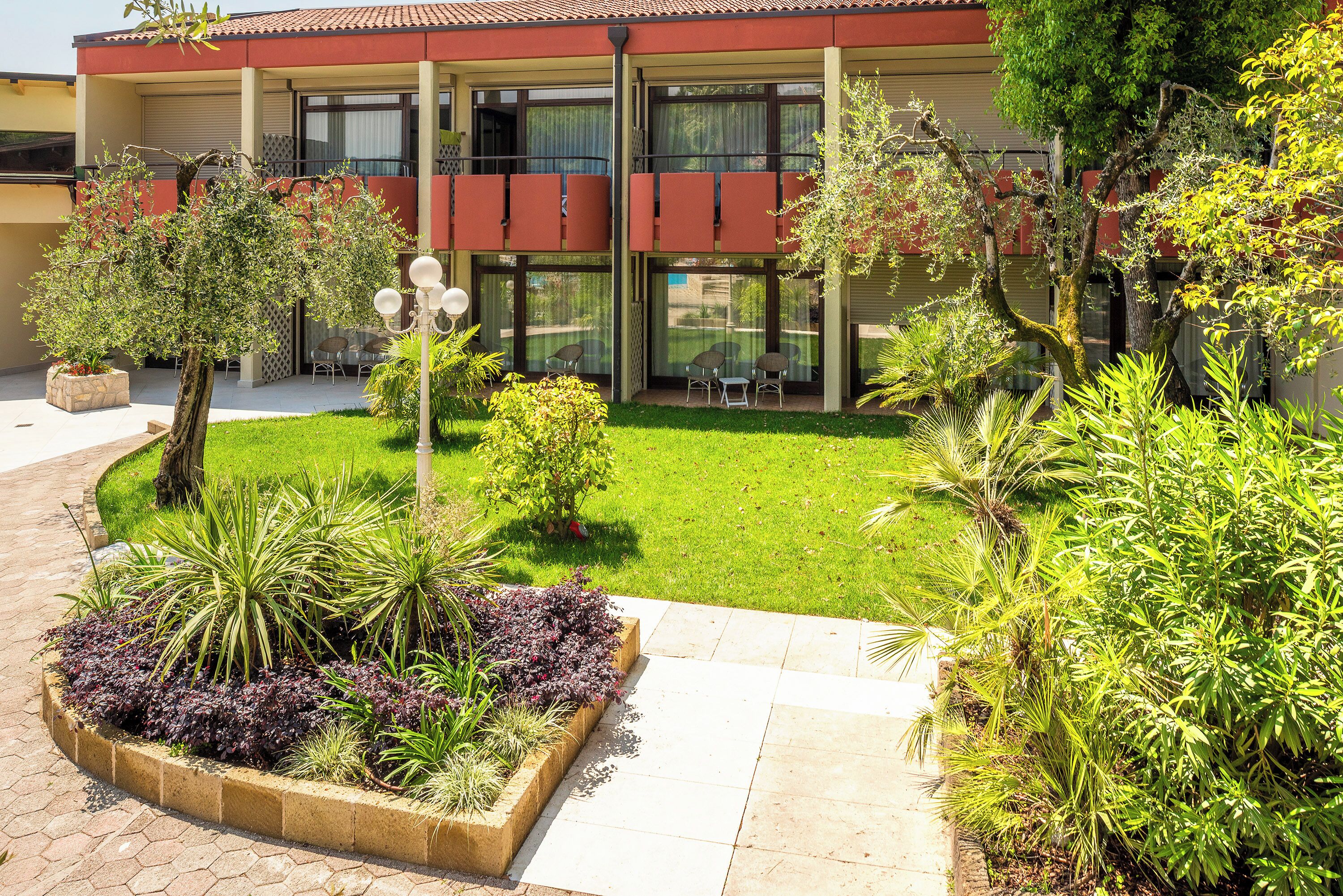 A building with a red facade, large windows, and a well-maintained garden with various plants and a seating area.