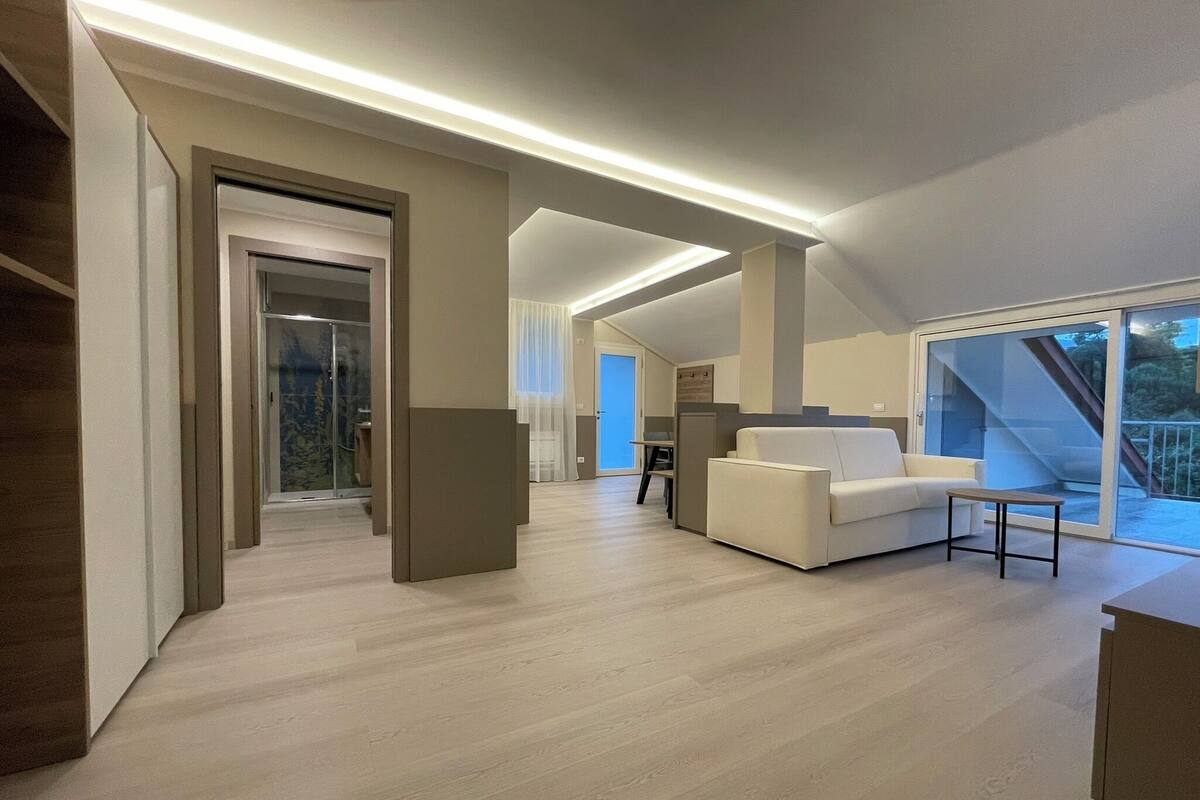 Un intérieur moderne avec un escalier menant à un balcon, un canapé blanc et un coin repas.