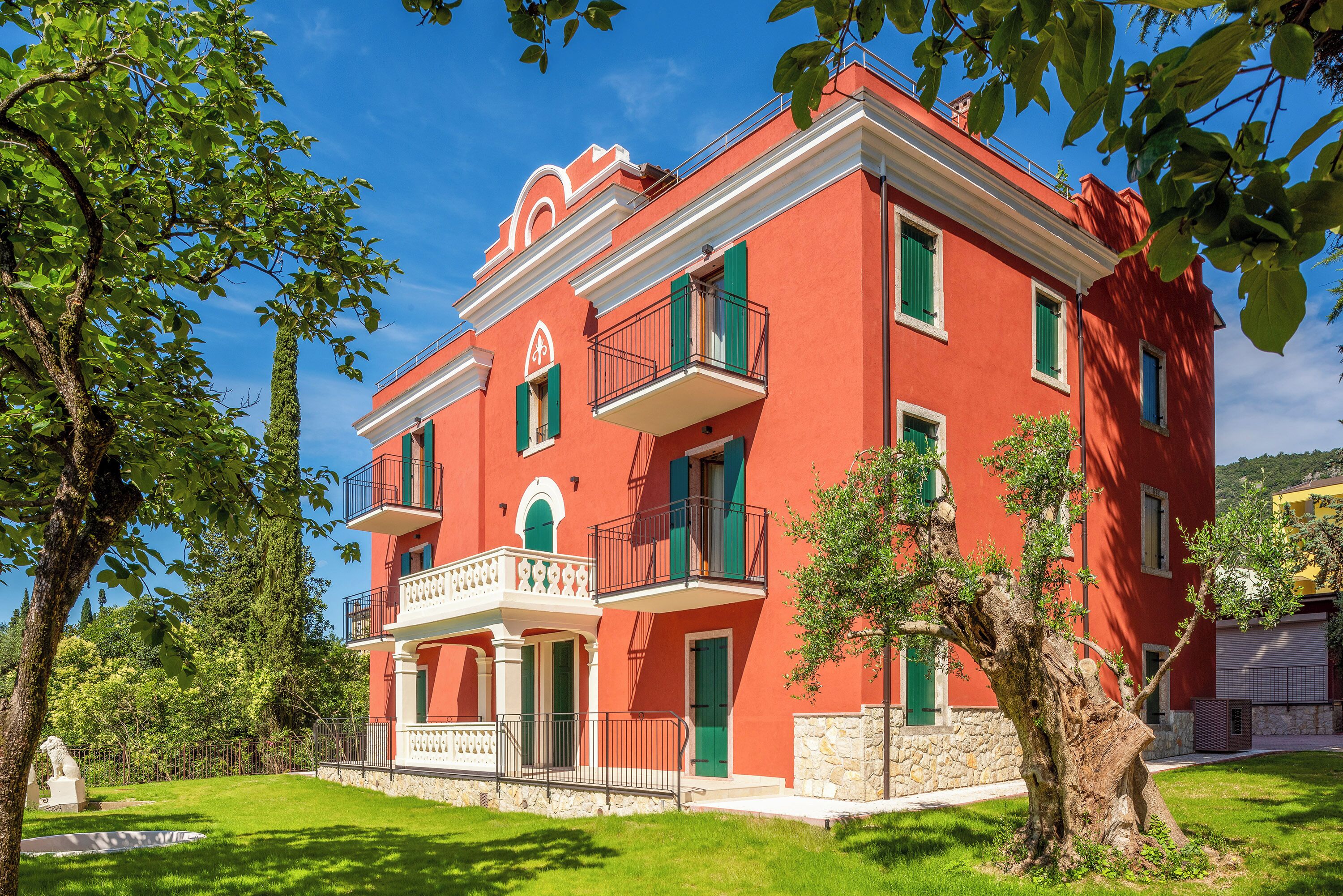 A red building with green shutters, a balcony, and a stone base.