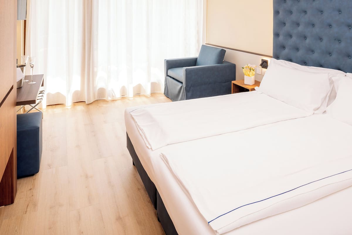 Une chambre d’hôtel avec un lit, un bureau, une chaise et une fenêtre avec des rideaux.