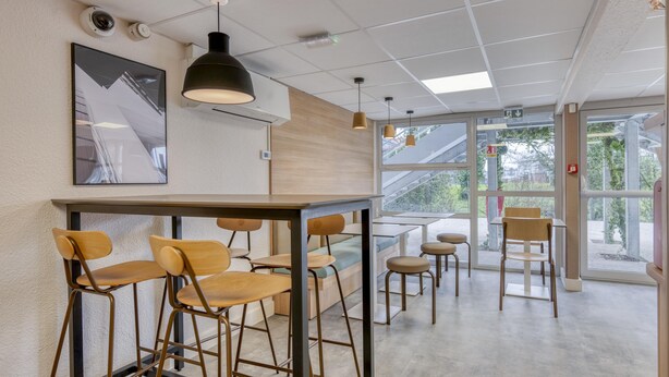 A modern interior with a bar area, seating, and large windows. - Premiere Classe Limoges Nord (Limoges)