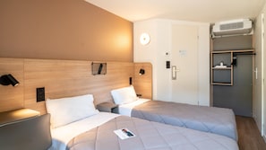 A hotel room with two beds, a wooden headboard, bedside lamps, a wall-mounted clock, and an air conditioning unit. - Premiere Classe Limoges Nord (Limoges)