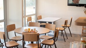 A dining area with round tables and chairs, a television mounted on the wall, and a window providing natural light. - Premiere Classe Limoges Nord (Limoges)