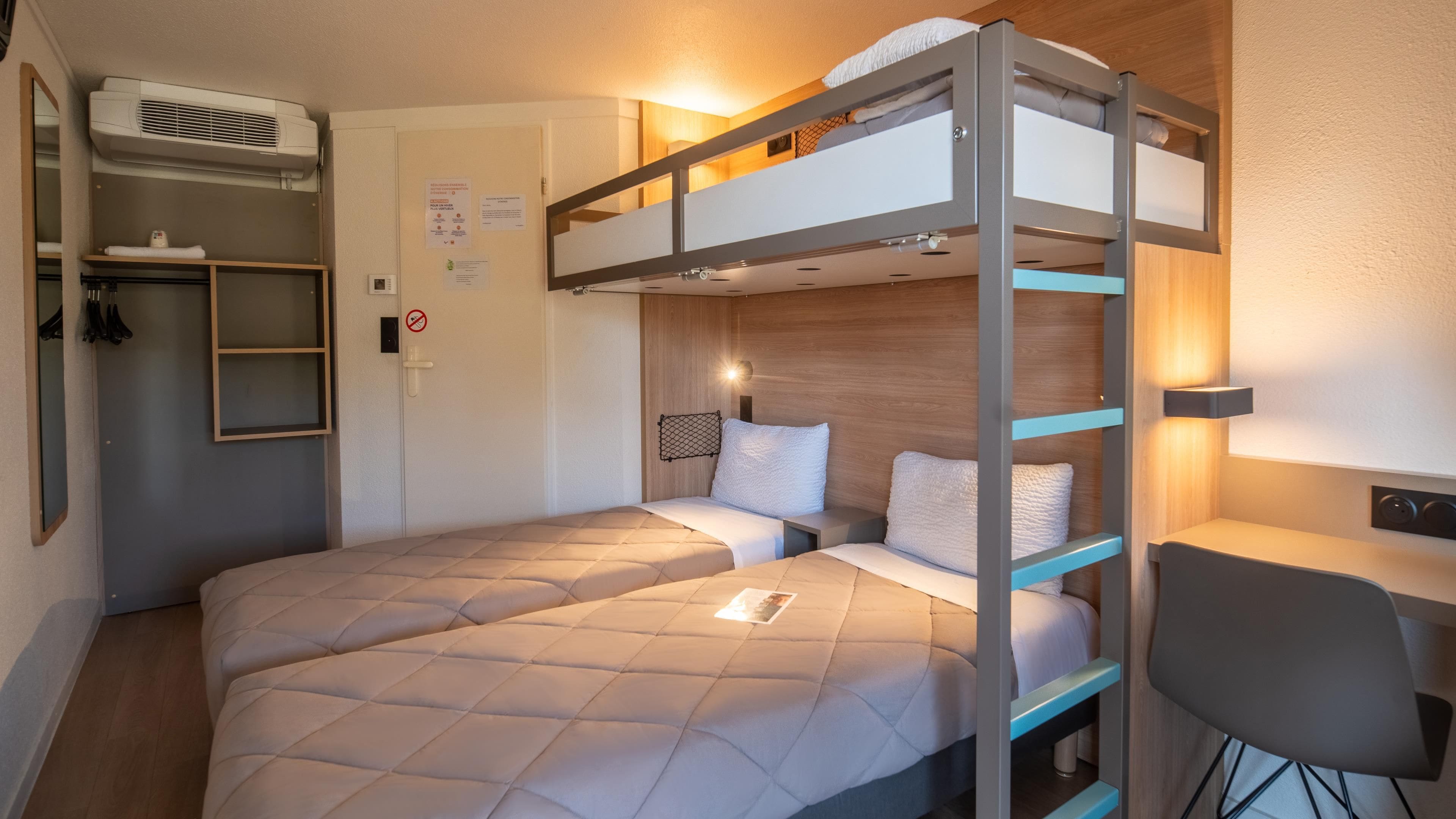 Een slaapkamer met een stapelbed, bureau en stoel, een spiegel en een kledingkast.