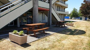 A building with a staircase leading to a balcony, outdoor wooden picnic tables, and planters with small plants. - Premiere Classe Limoges Nord (Limoges)
