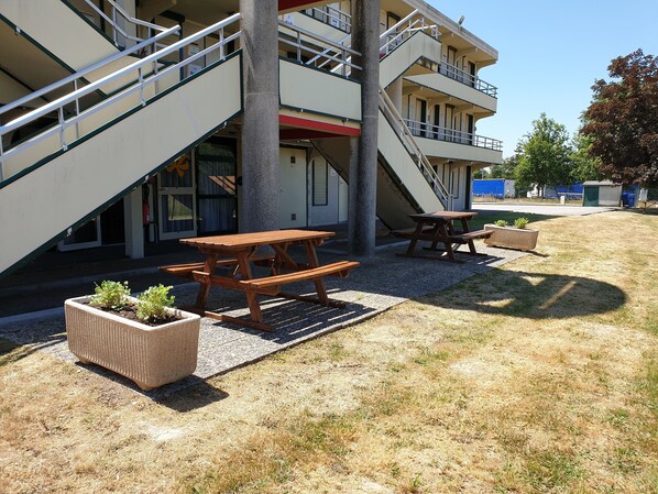 A building with a staircase leading to a balcony, outdoor wooden picnic tables, and planters with small plants.