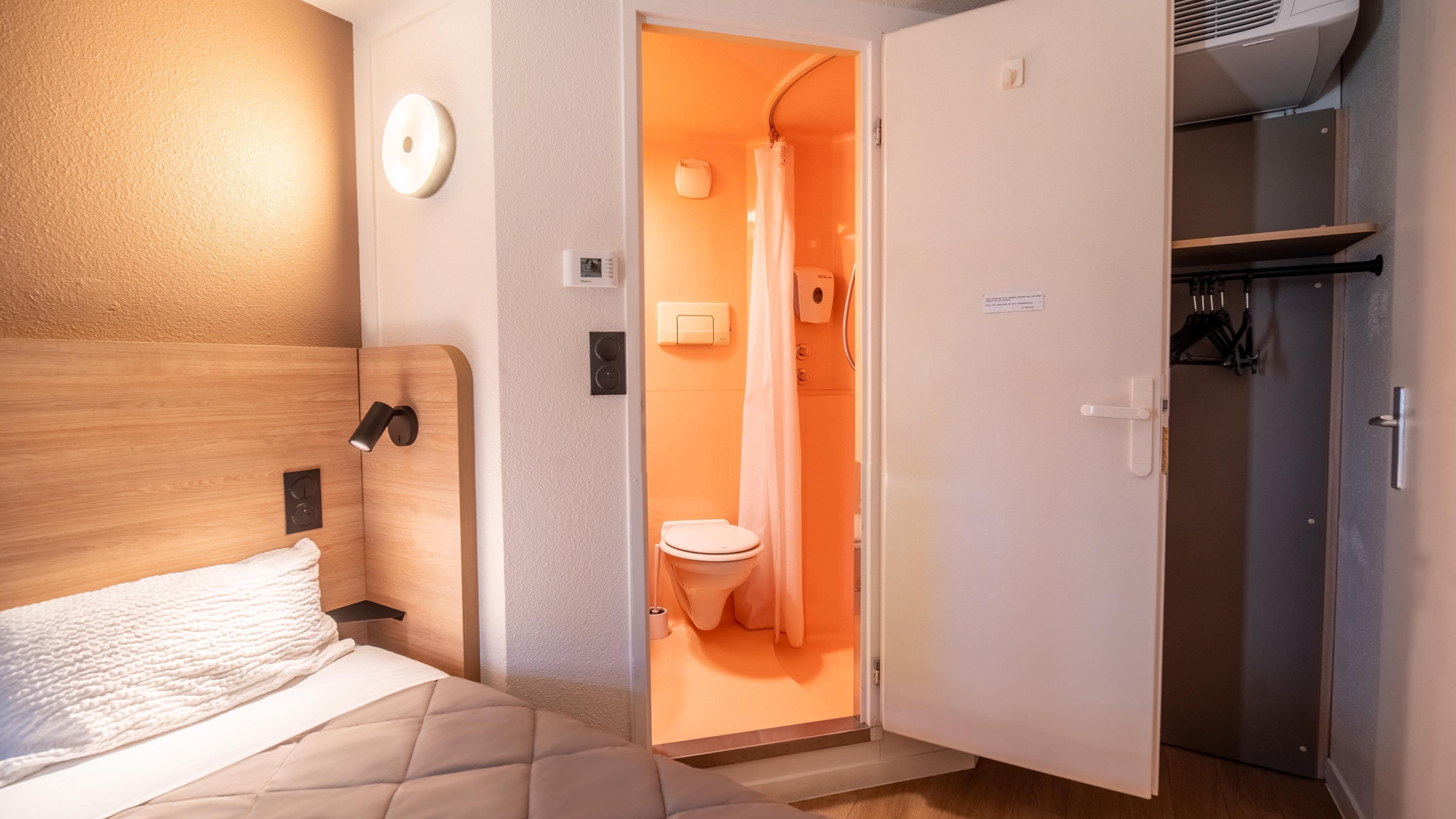 Quarto com cama, cabeceira de madeira, mesa de cabeceira e luminária fixada na parede.