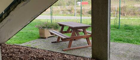 A covered outdoor area with a picnic table and benches, surrounded by a gravel path and mulch.
