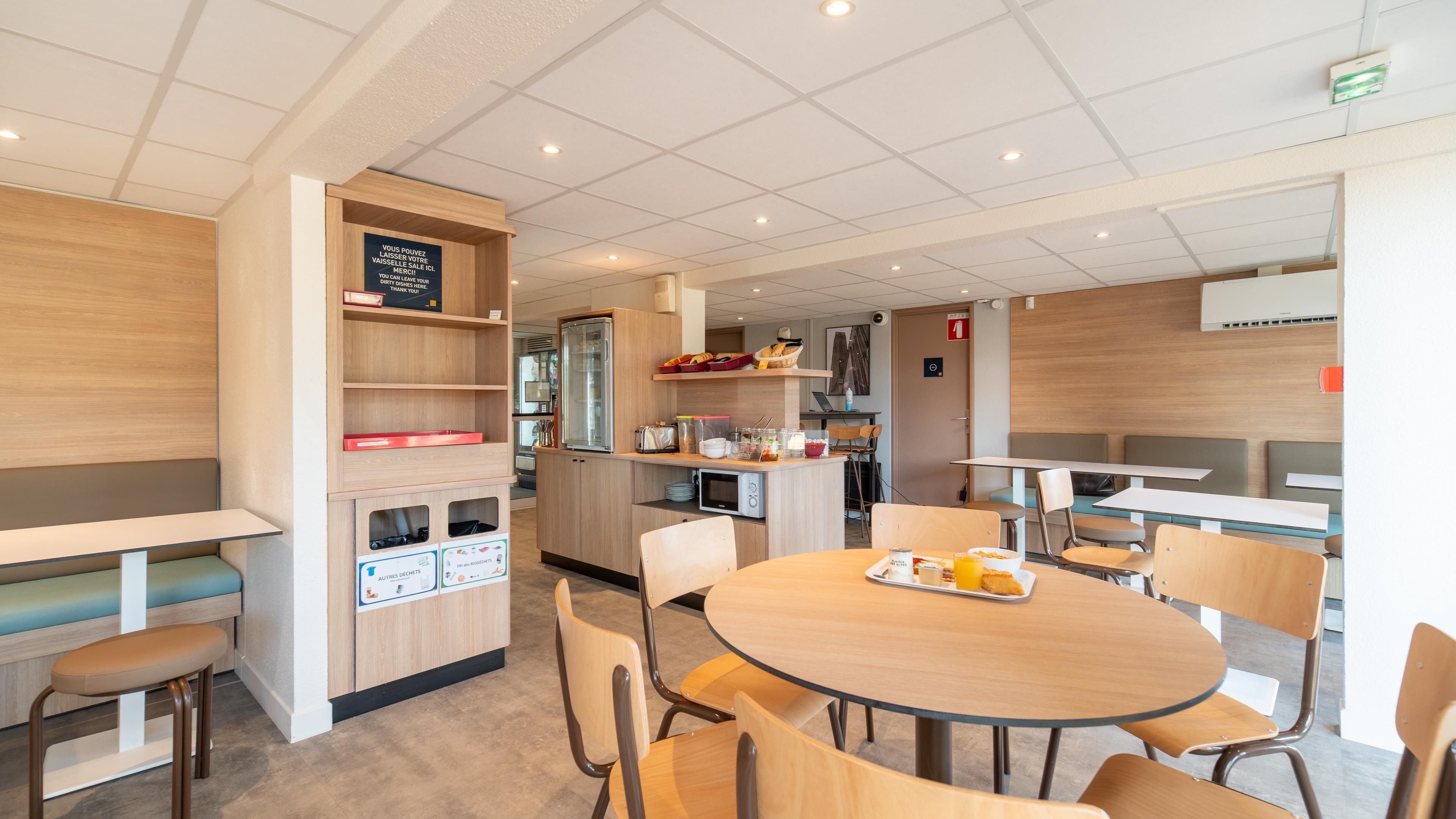 Una cafetería moderna con mesas y sillas redondas, una barra con productos alimenticios y una pared de madera con estantería.
