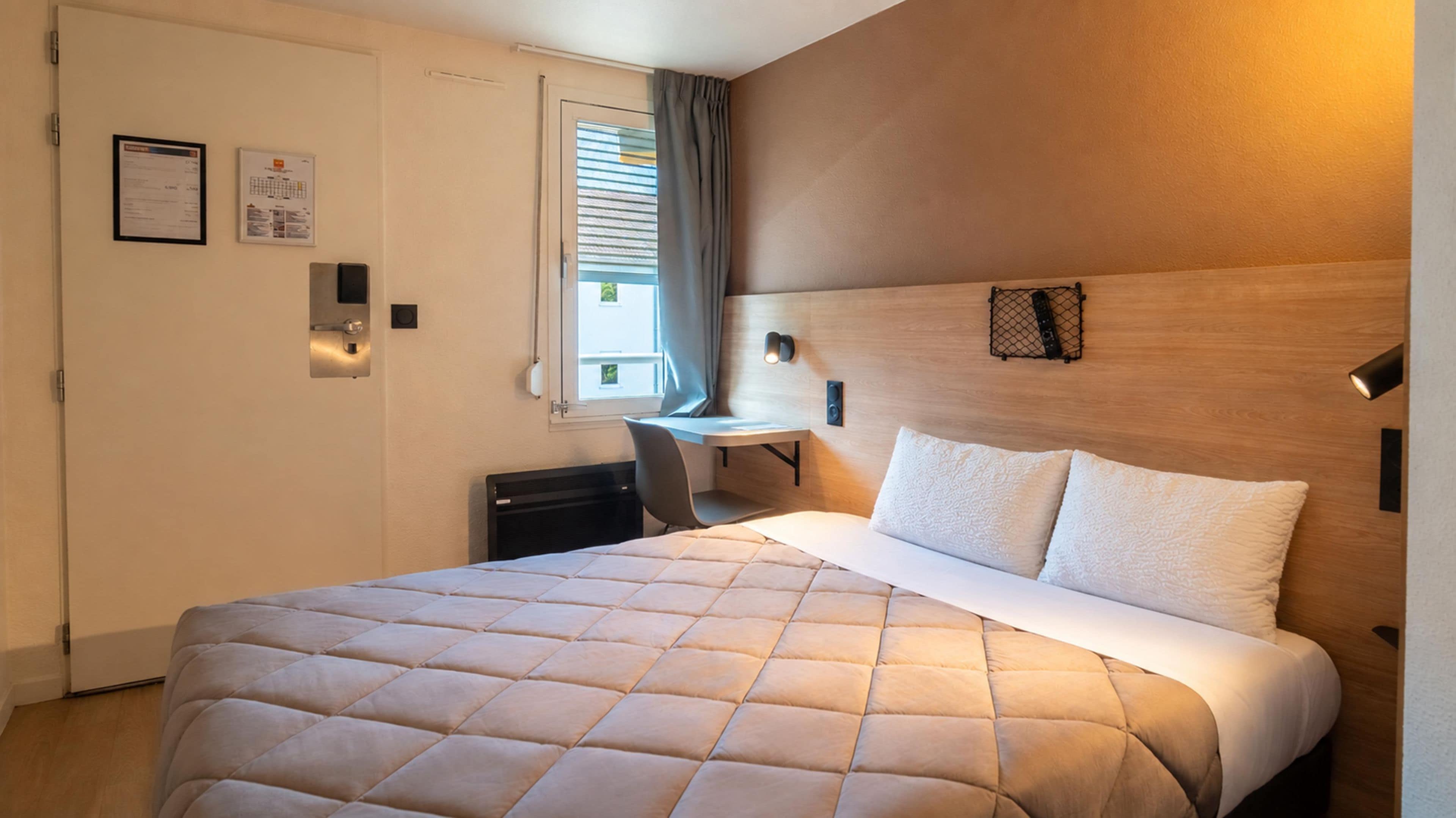 A hotel room with a bed, a desk, and a chair.