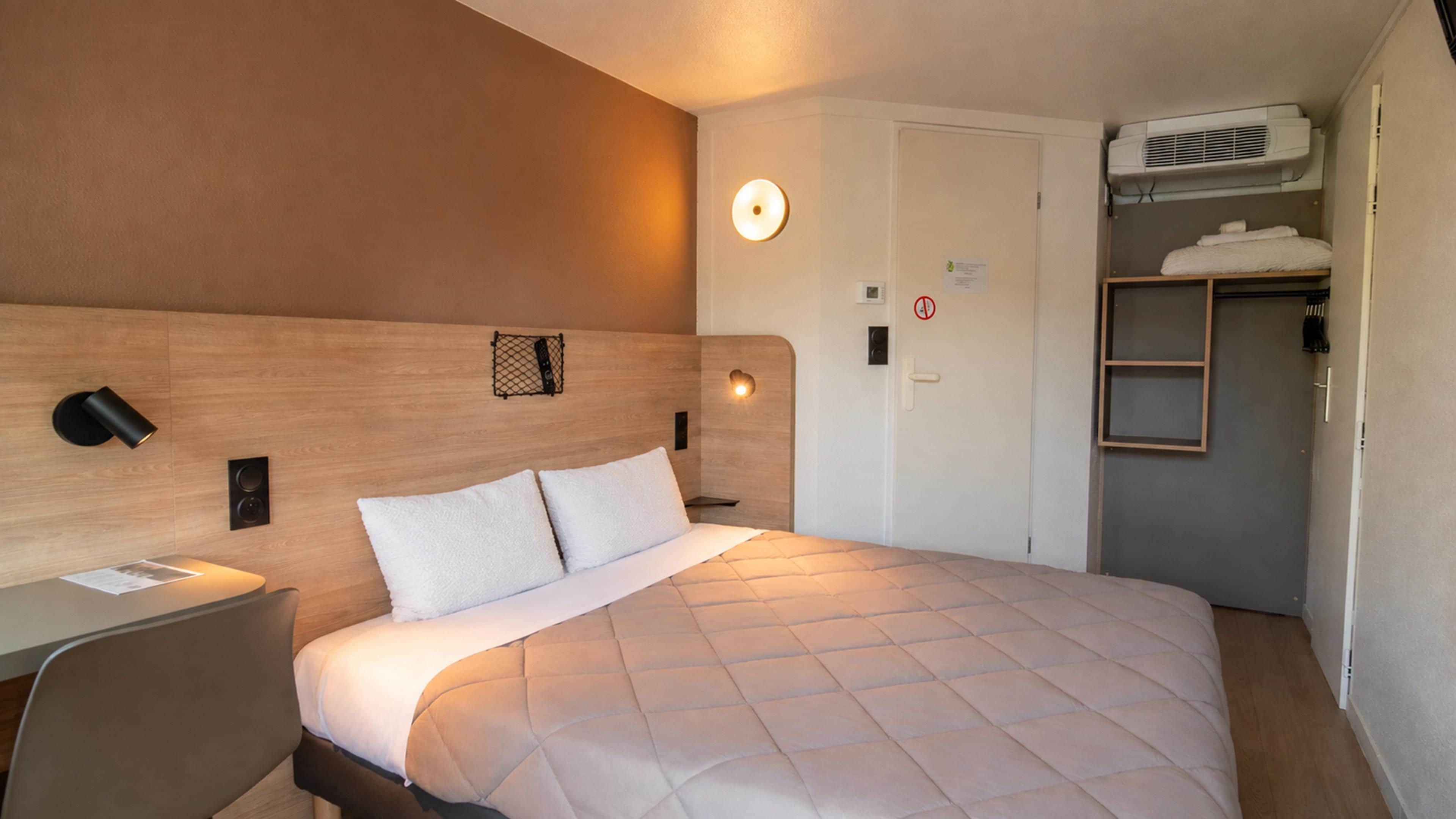 Ein Hotelzimmer mit Bett, Nachttisch, Wandlampe und einer Tür mit Rauchverbot-Schild.