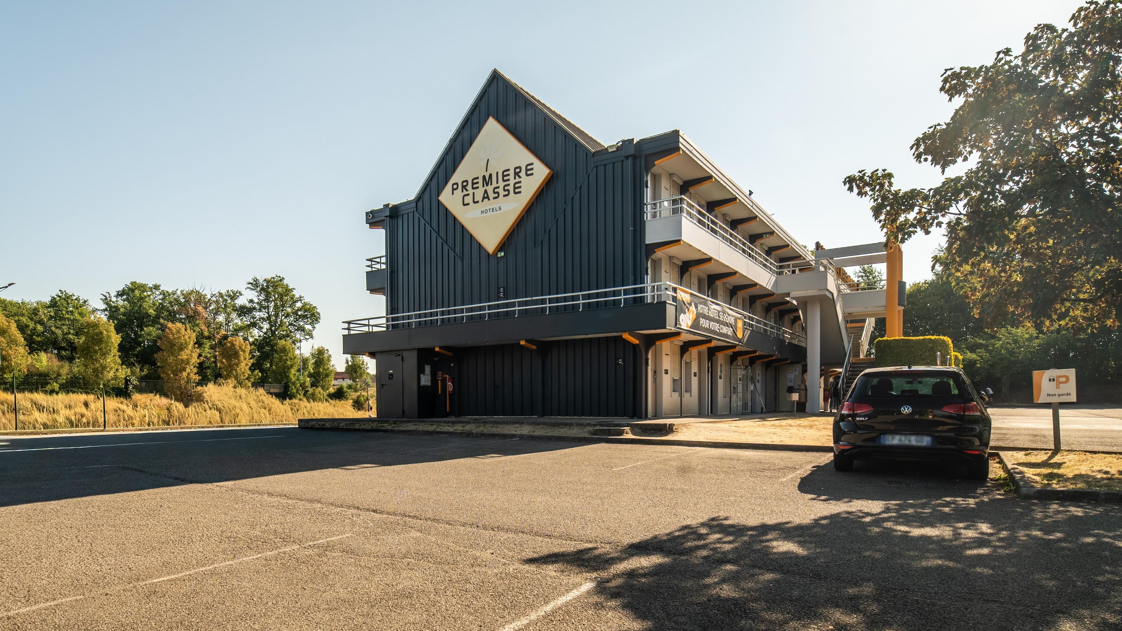 Een modern hotel met een opvallend bord waarop 'Première Classe Hotels' staat en een parkeerplaats met een auto.