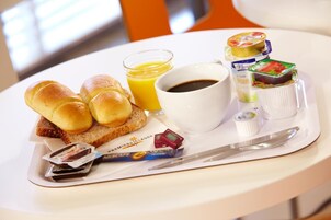 Bandeja de desayuno con panecillos, un vaso de zumo de naranja, una taza de café y diversos condimentos y salsas.