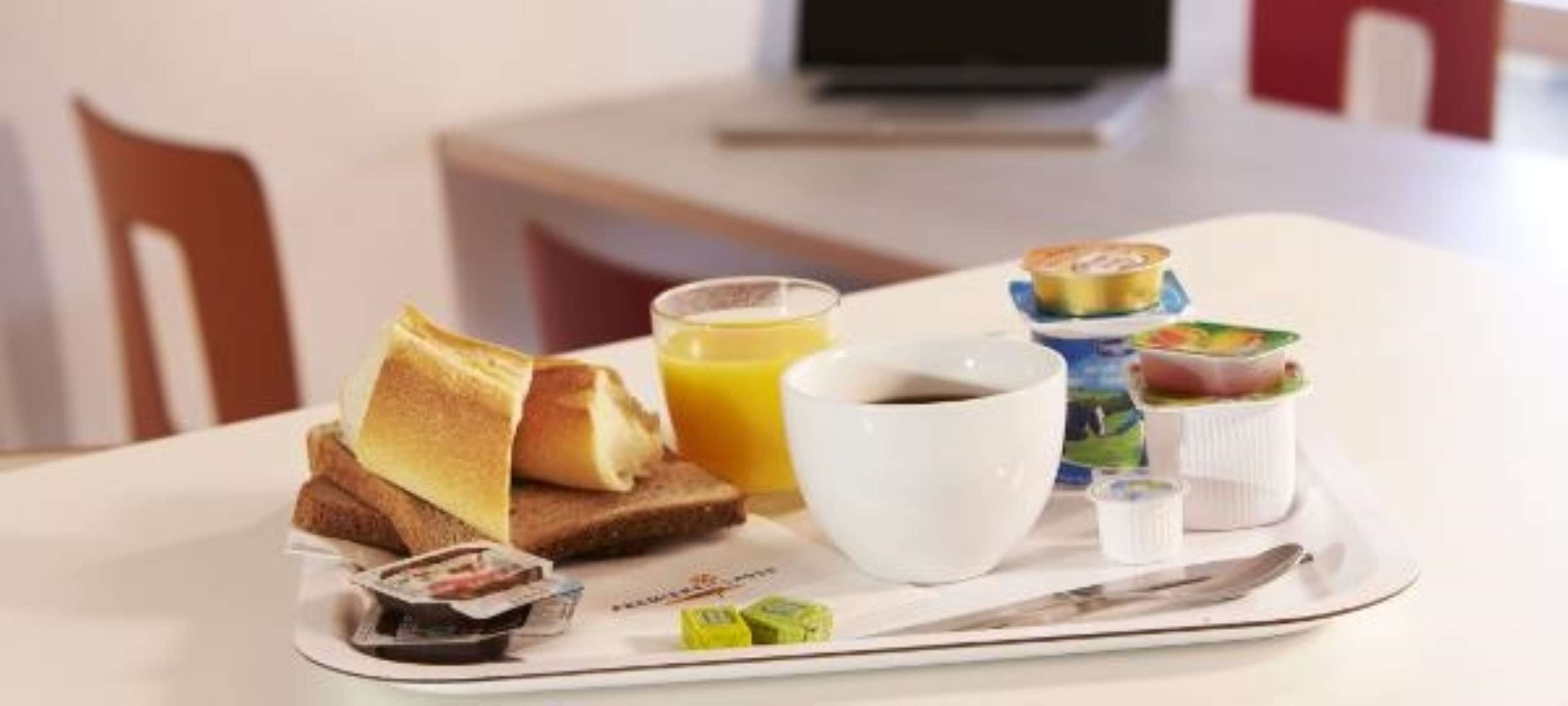 A breakfast tray with toast, orange juice, coffee, yogurt, and a small container of jam.