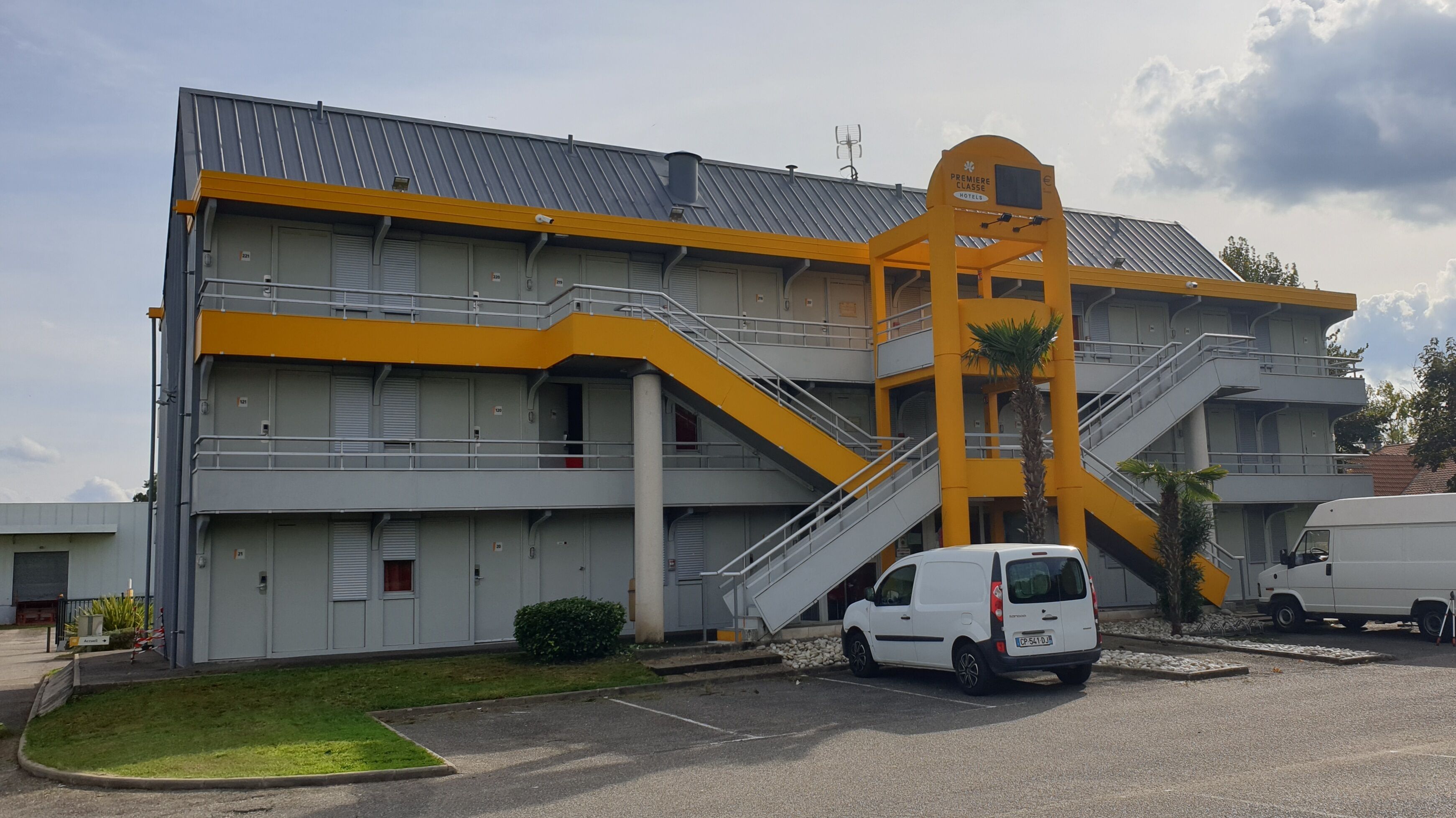 Un immeuble à plusieurs étages aux couleurs jaune et gris, doté d’un escalier imposant et d’une enseigne indiquant qu’il s’agit d’un hôtel.