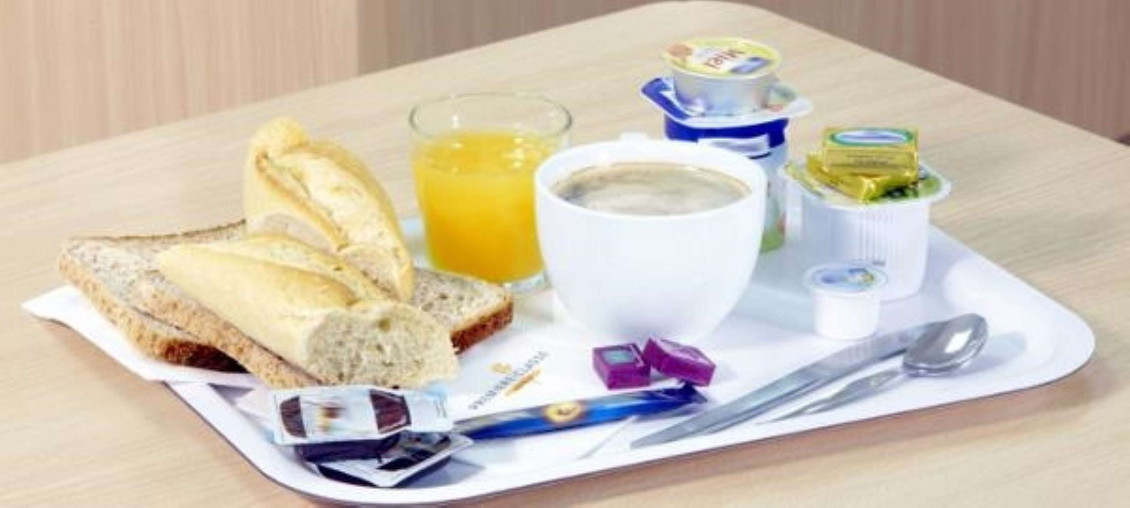 Bandeja de desayuno con pan, jugo, yogur y una taza de café.